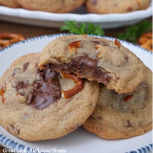 A white round plate with blue trim with four brown butter pretzel toffee cookies on it with a bite out of the cookie on top.
