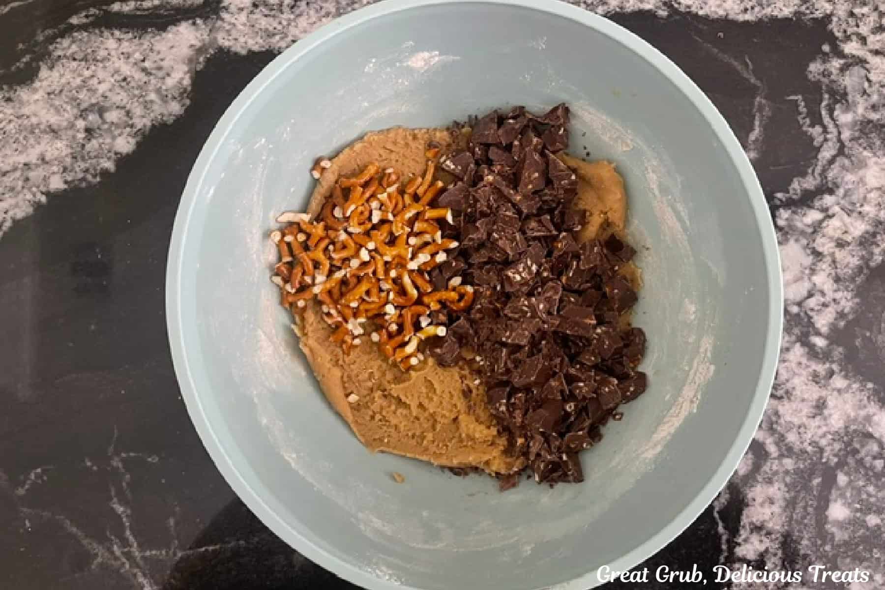 A mixing bowl with chopped chocolate pieces and coarsely chopped pretzels added to the cookie batter before being stirred together.