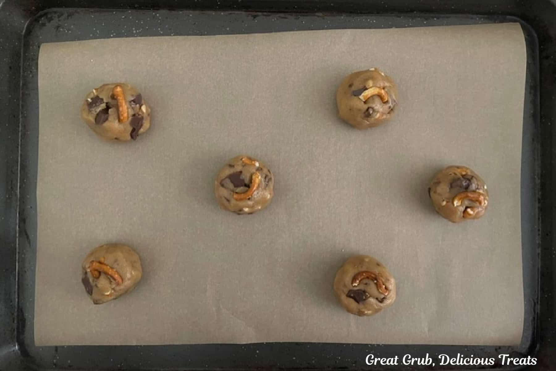 A parchment paper lined baking sheet with six cookie dough balls on it before going in the oven.