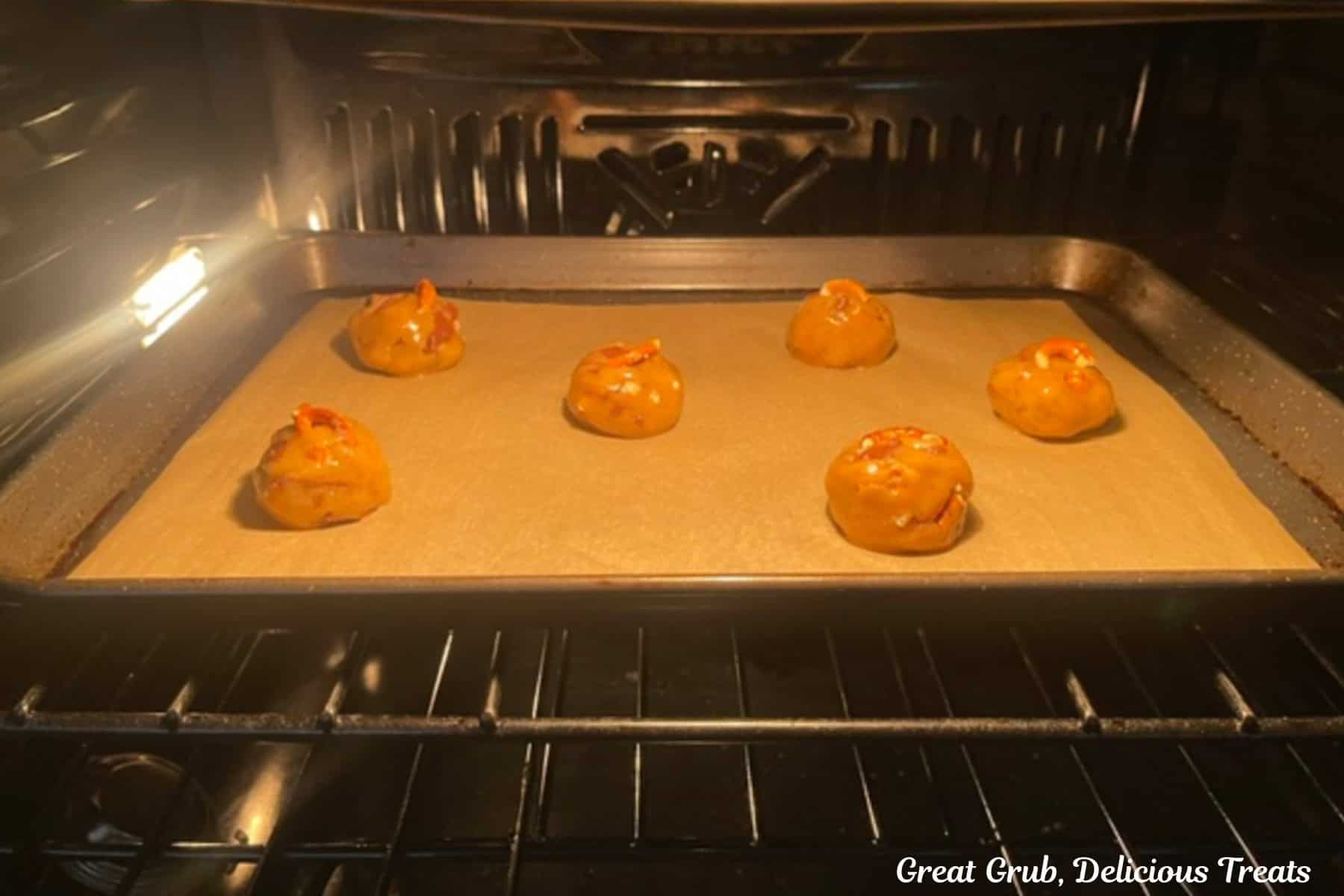 A baking sheet with six cookie dough balls on it baking.