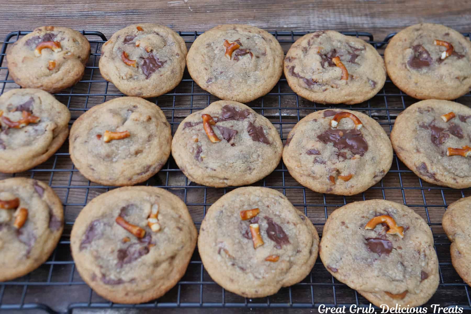 A wire rack with fifteen brown butter pretzel toffee cookies cooling on it.