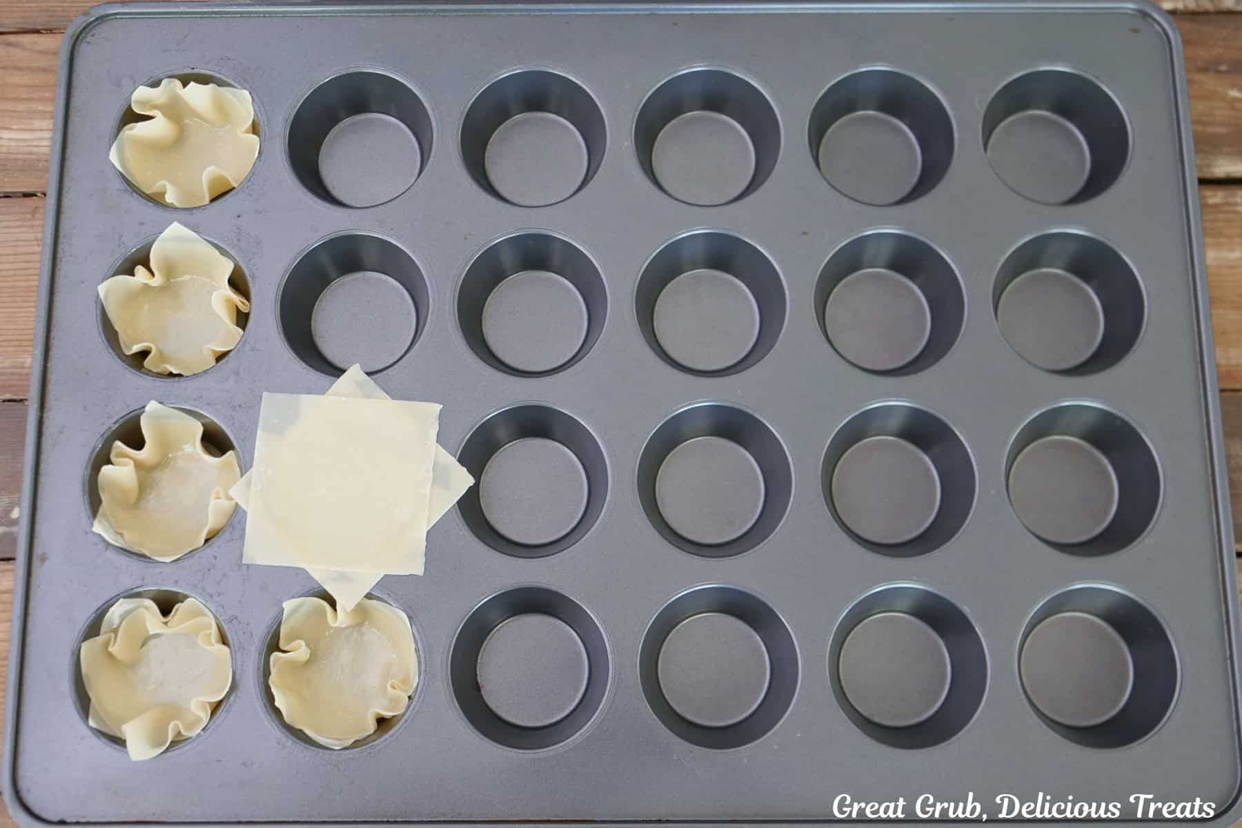 A 24-count muffin tin with wonton wrappers placed in some of the openings, and two wrappers placed on top of each other.