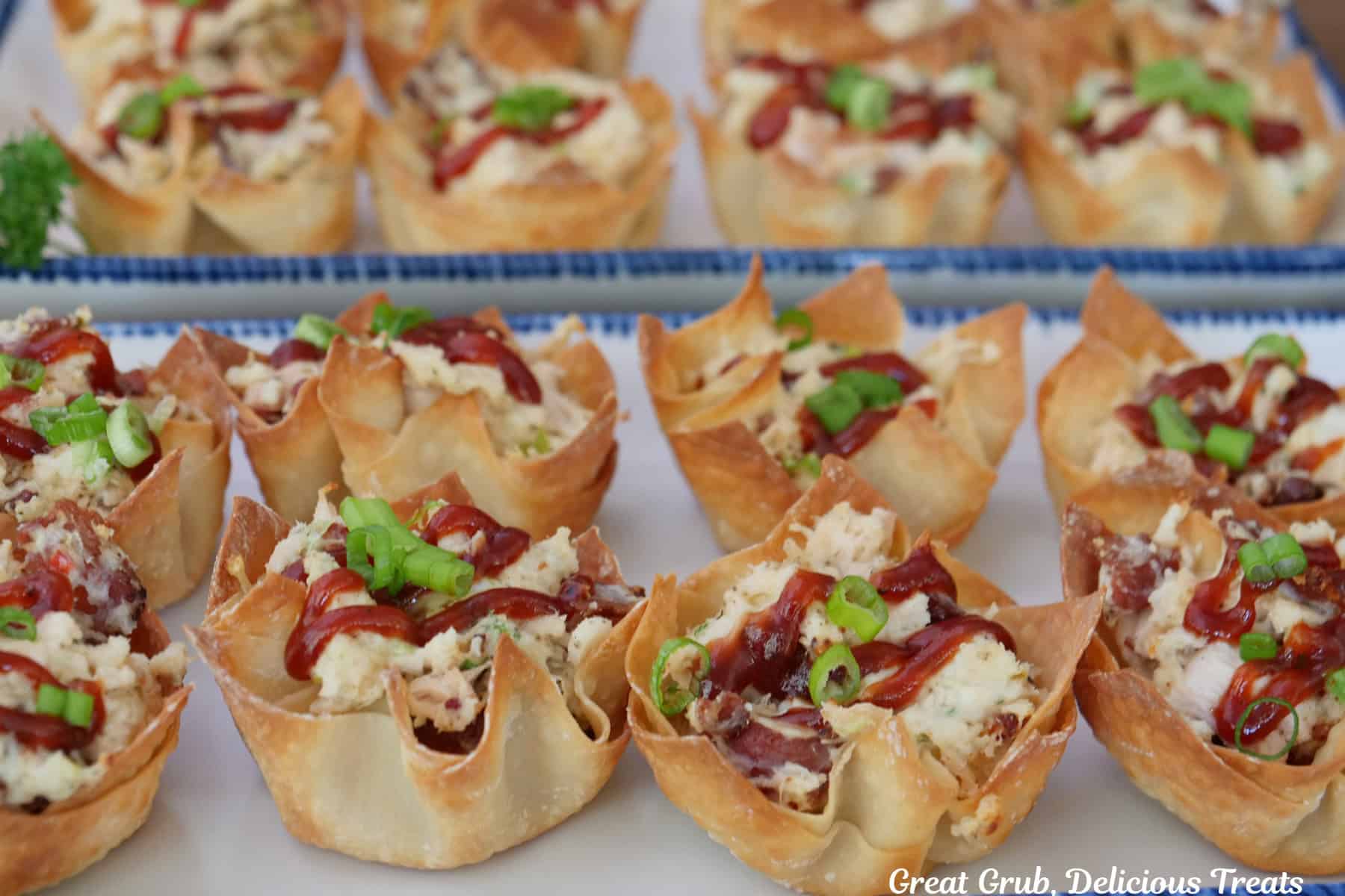 Two oblong white plates with blue trim with eight chicken bacon ranch wonton cups on each plate.