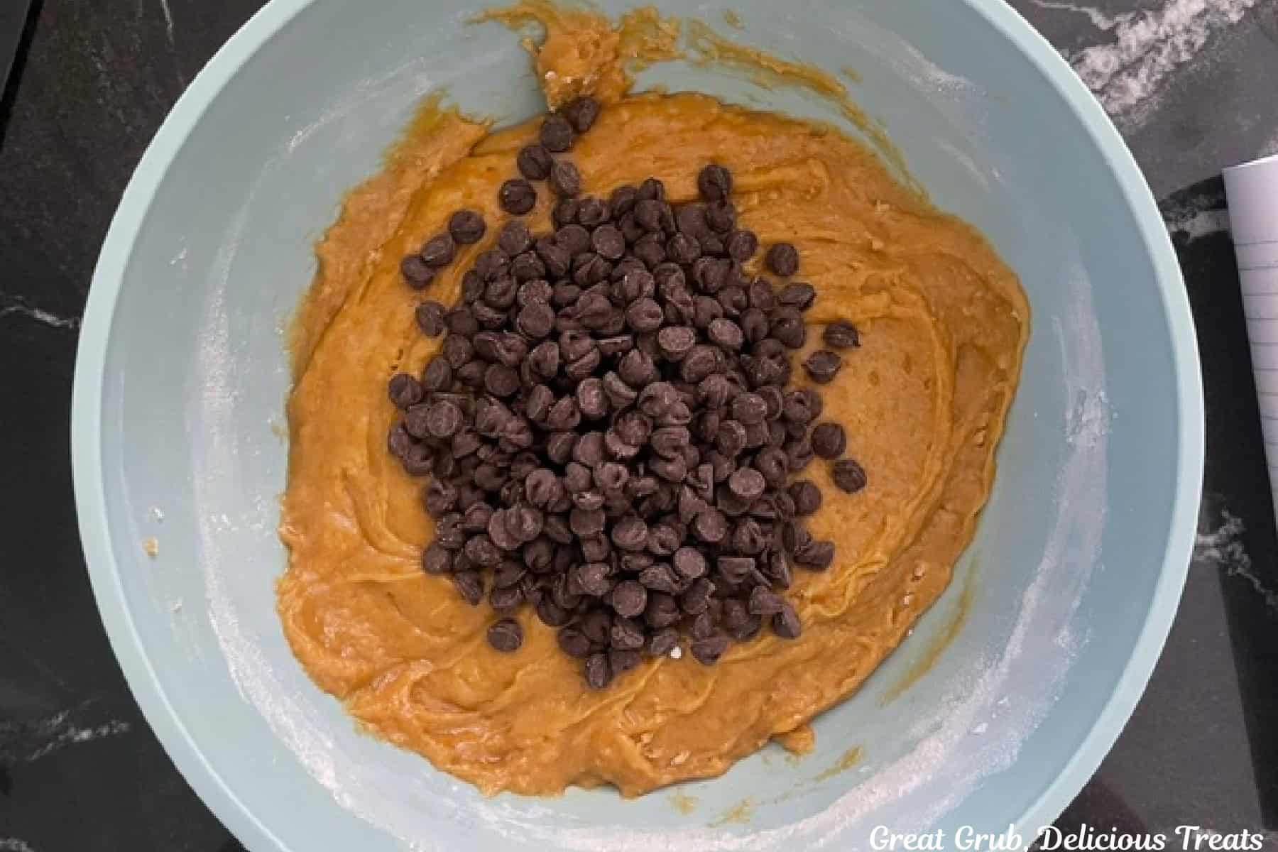 A mixing bowl with pumpkin cookie dough and chocolate chips added before being mixed together.