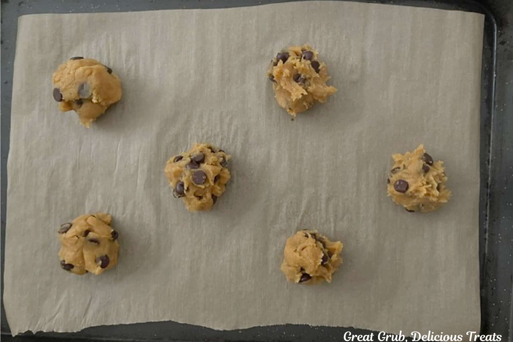 A parchment paper lined baking sheet with six chocolate chip pumpkin cookie dough balls on it before being baked.