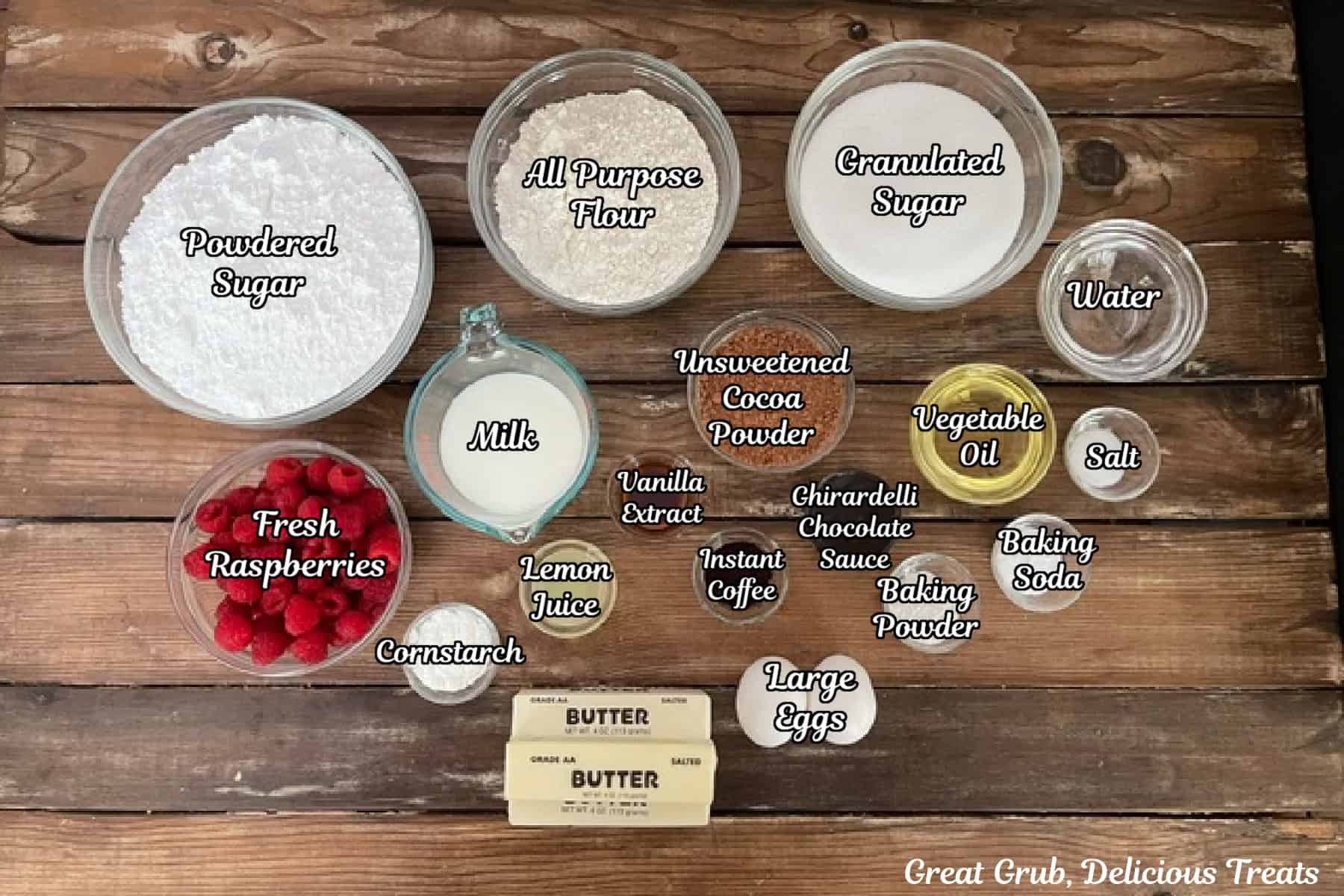 A rustic wood surface with all the ingredients placed on it to make chocolate cupcakes with raspberry buttercream frosting.