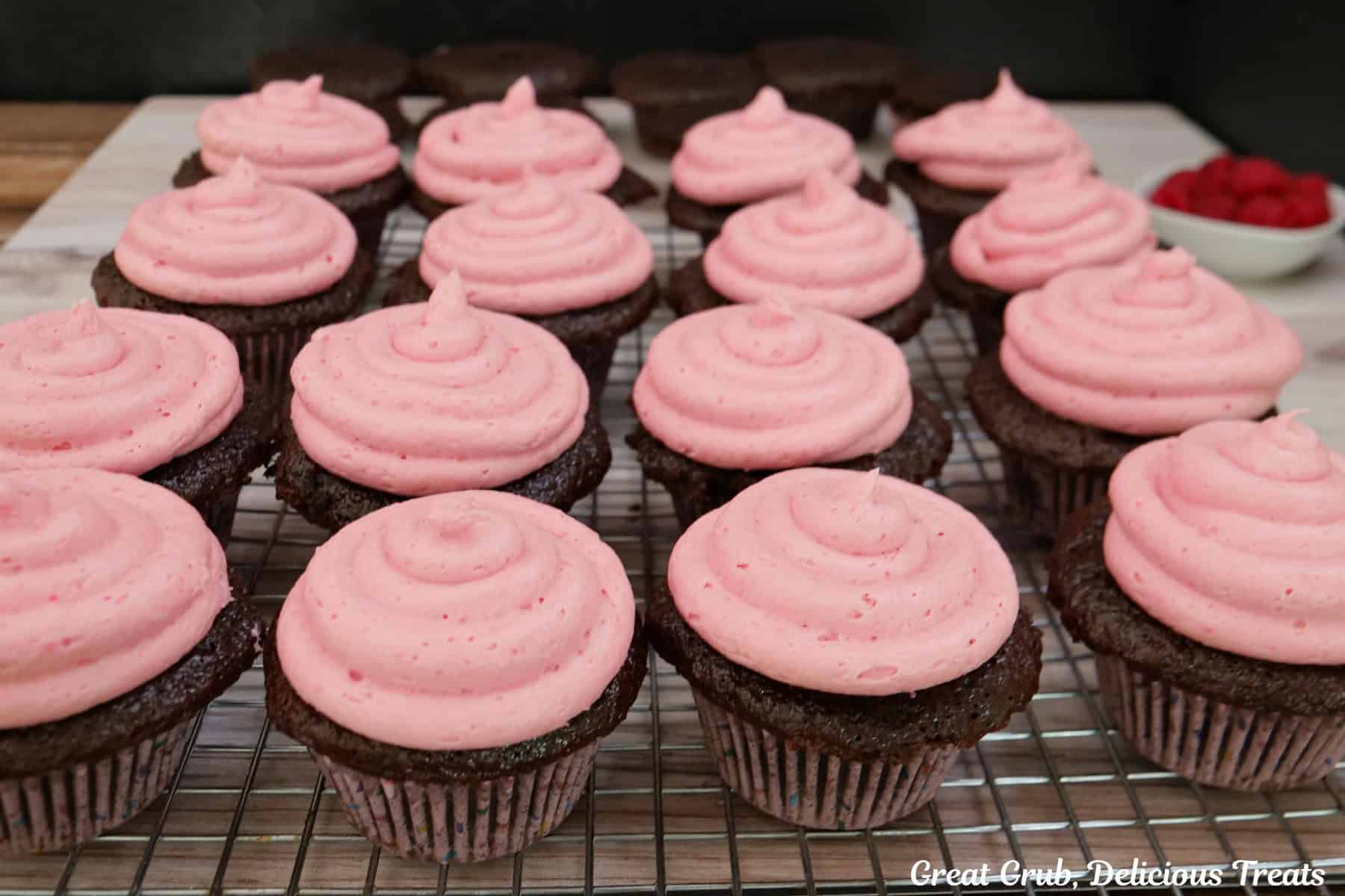 A wire rack with frosted chocolate cupcakes it.