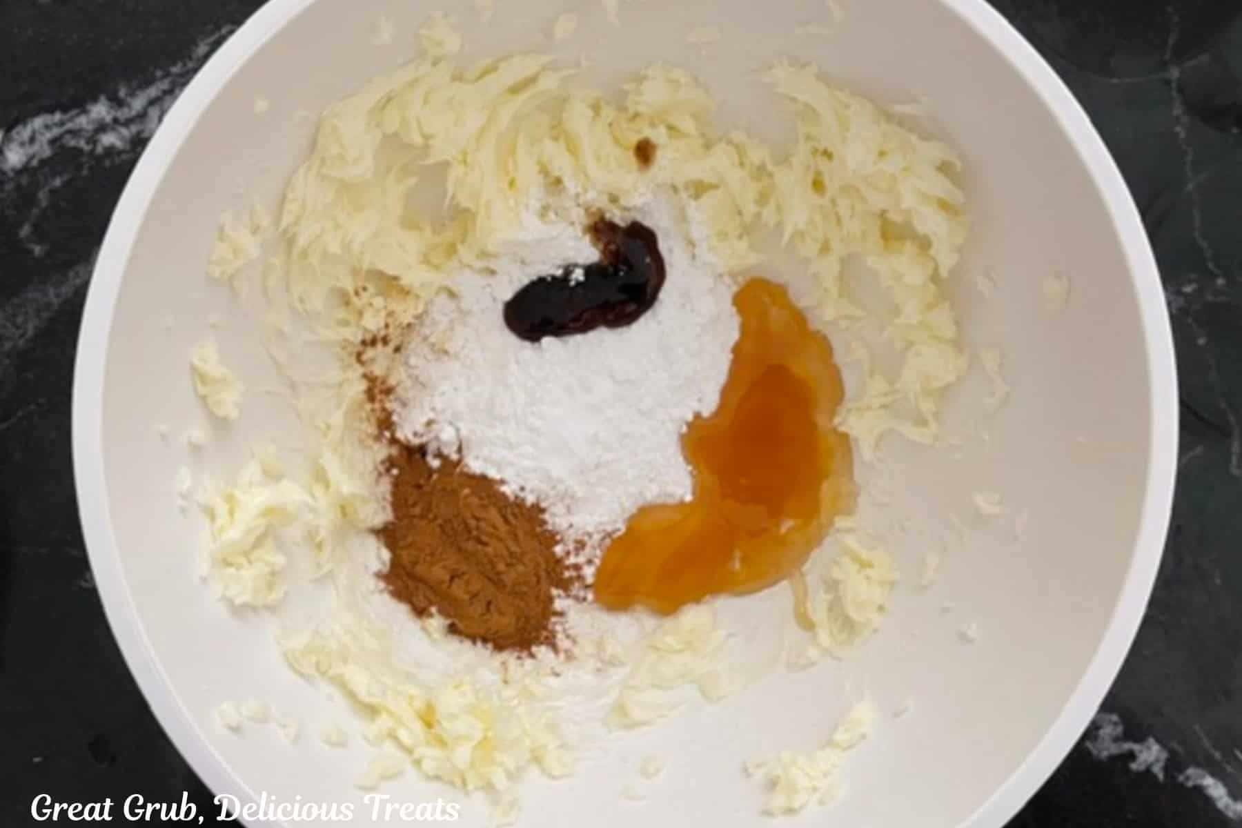 A white mixing bowl with butter, honey, cinnamon, vanilla bean paste, powdered sugar, and salt in it before being mixed together.