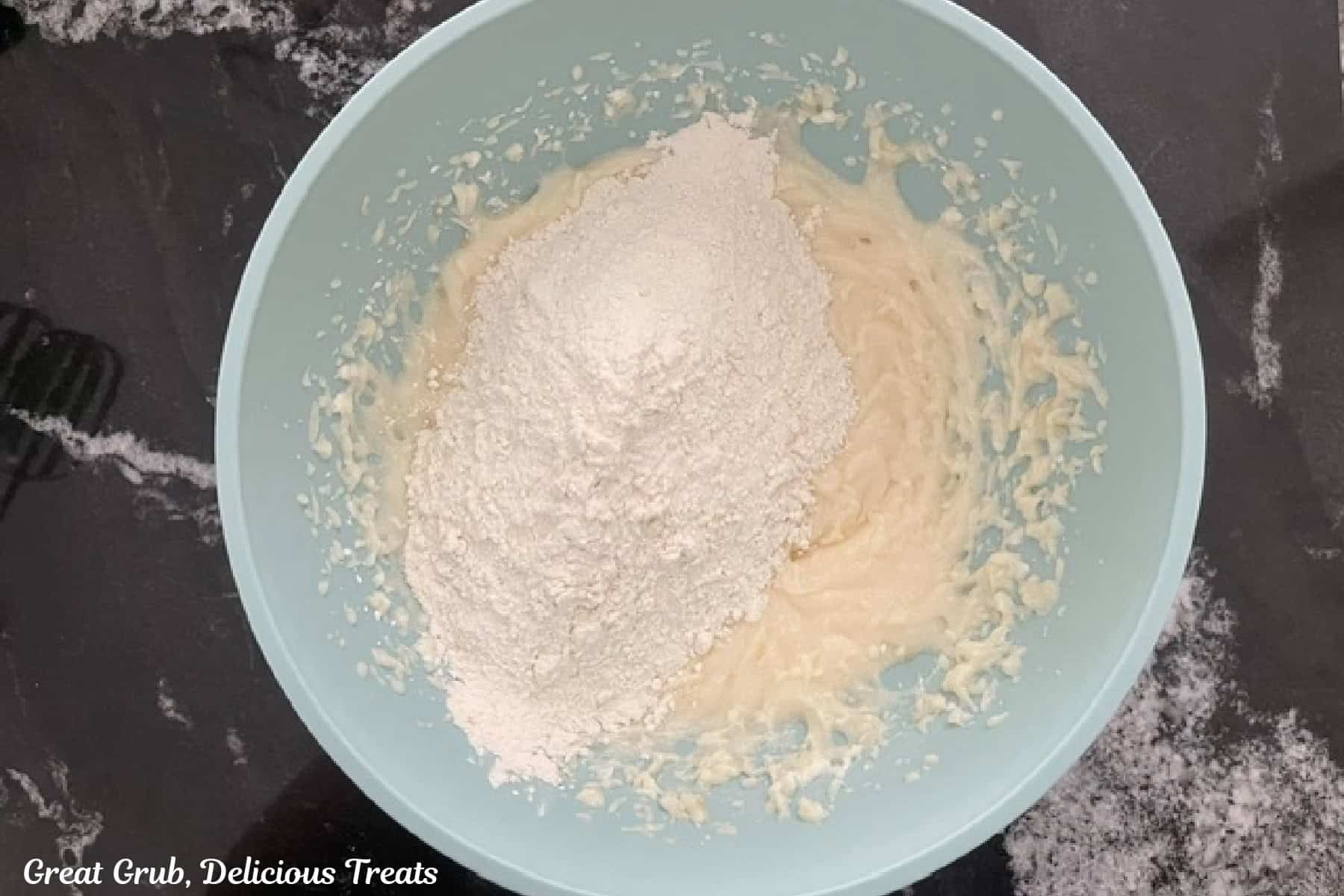A mixing bowl with dry cookie ingredients being added to the wet cookie batter ingredients.