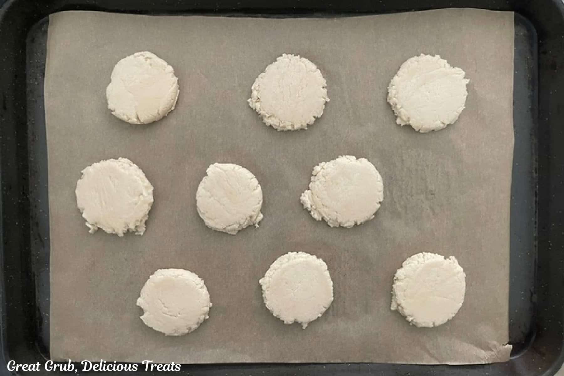 A parchment lined baking sheet with nine eggless sugar cookies placed on it before being baked.