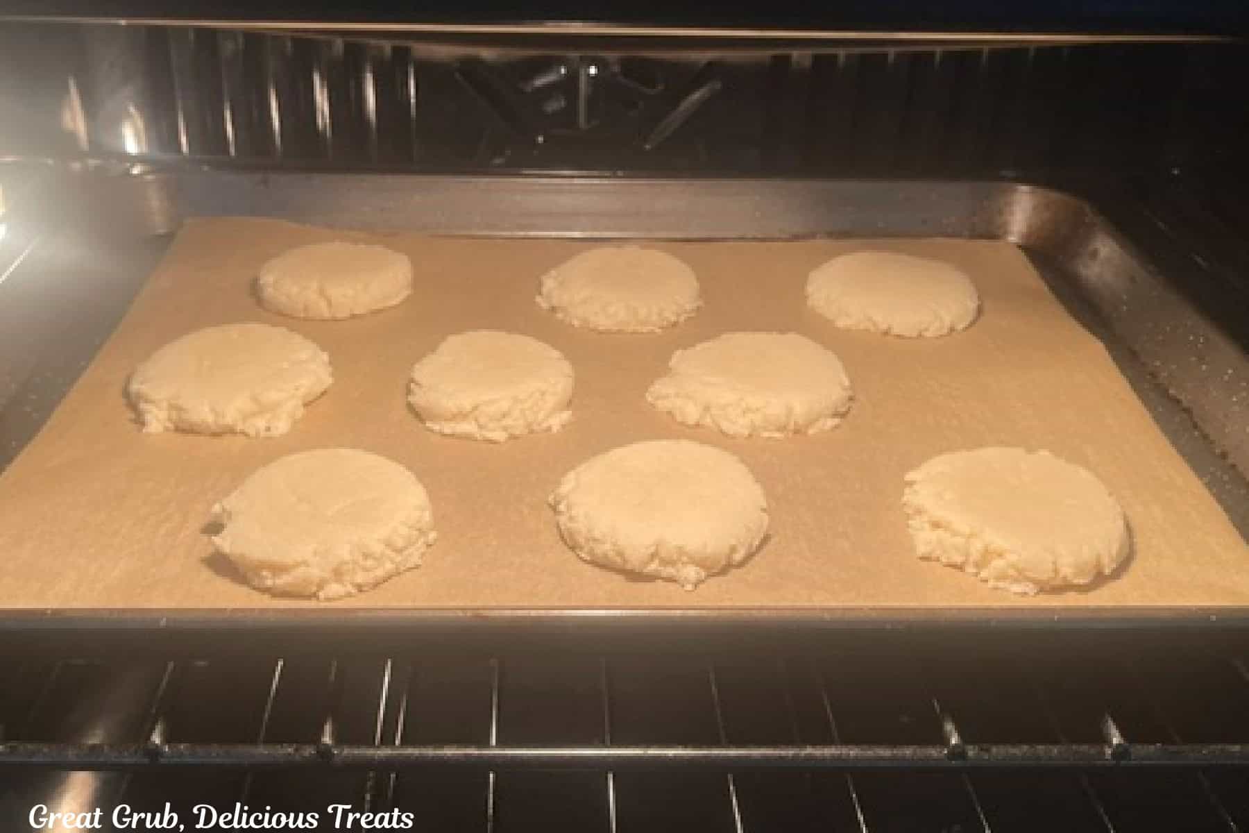 A baking sheet in the oven baking nine sugar cookies.