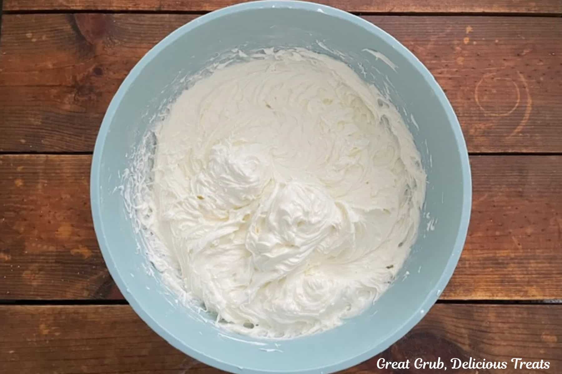 A wood surface with a light blue bowl filled with maple cream cheese frosting.