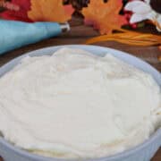 A wood surface with a light blue bowl filled with maple cream cheese frosting with fall foliage.