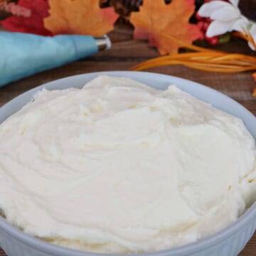 A wood surface with a light blue bowl filled with maple cream cheese frosting with fall foliage.