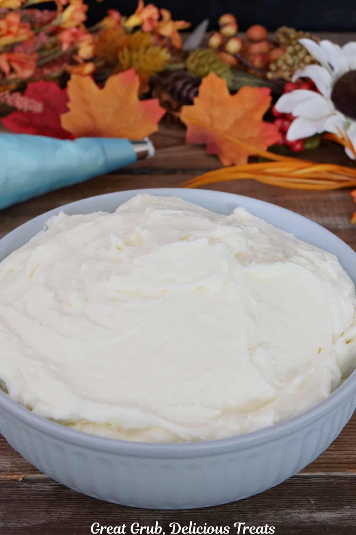 A wood surface with a light blue bowl filled with maple cream cheese frosting with fall foliage.