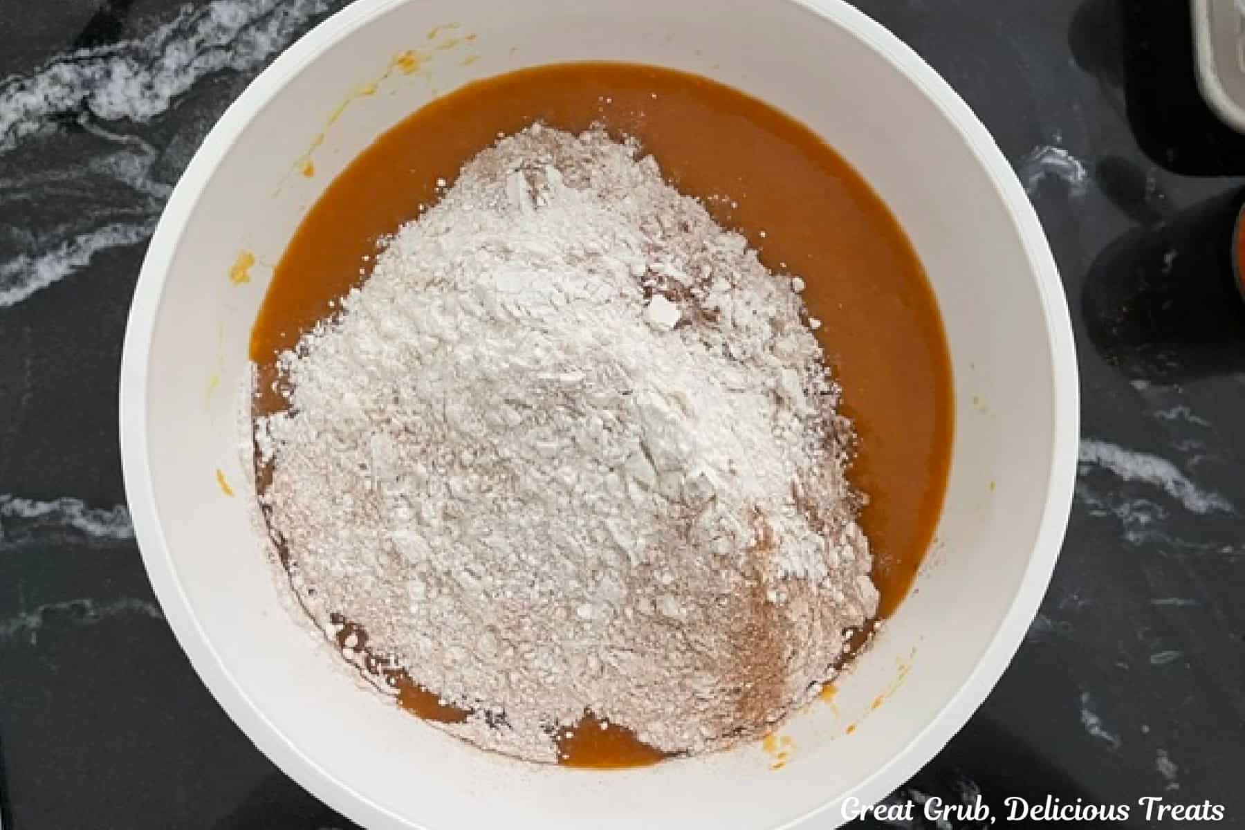 A white bowl with the wet pumpkin cupcake batter with the dry ingredients added to the bowl before being mixed together.