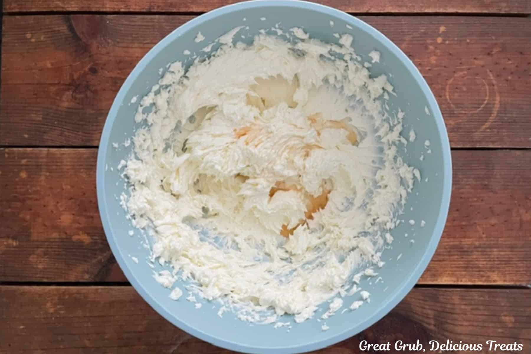 A light blue bowl filled with cream cheese and butter beaten together and maple extract added.