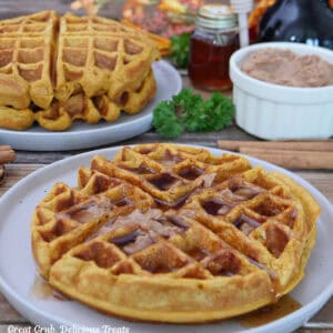A white plate with a large pumpkin spice waffle on it topped with cinnamon honey butter and maple syrup.