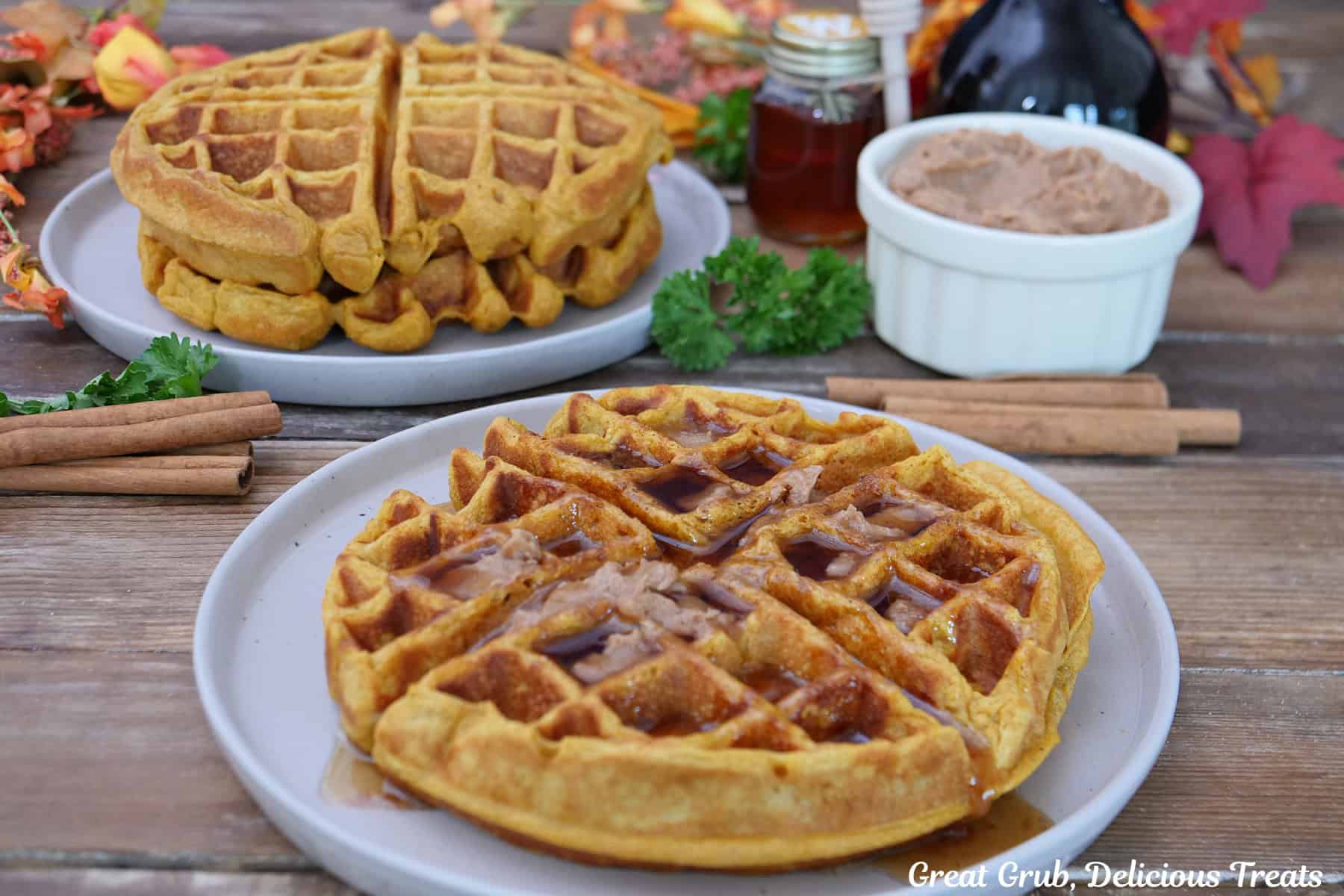 A wood surface with two white plates with pumpkin spice waffles on them.
