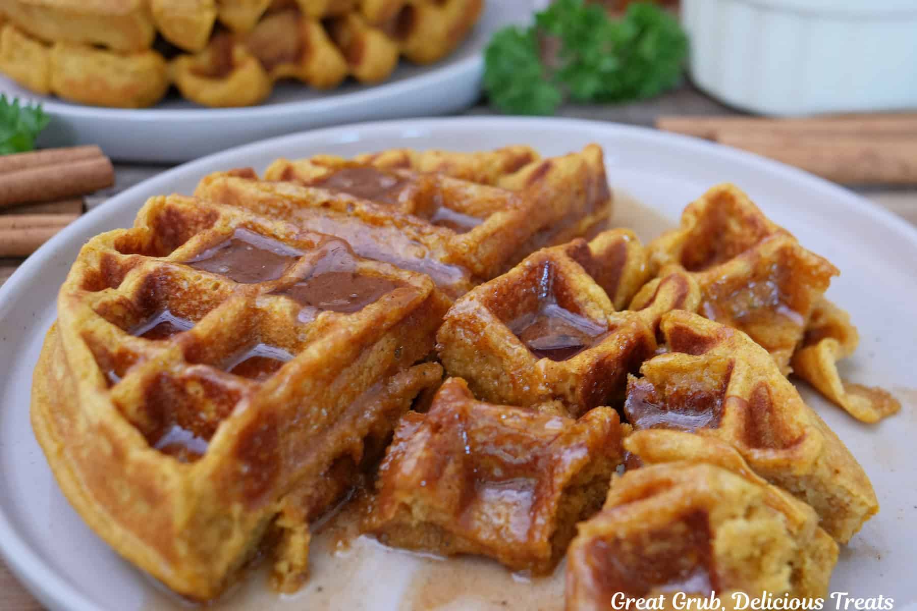 A white plate with a pumpkin spice waffle on it that has cinnamon honey butter and maple syrup on top and some cut into bite-size pieces.