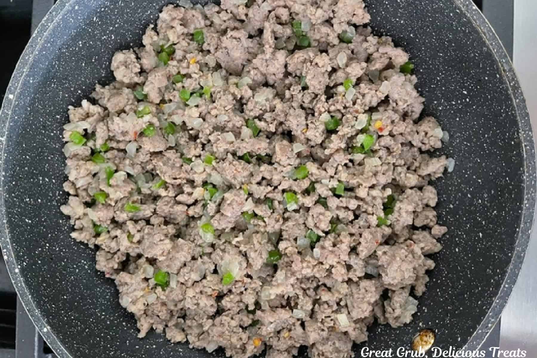 A pan with cooked sausage, onions, and peppers.