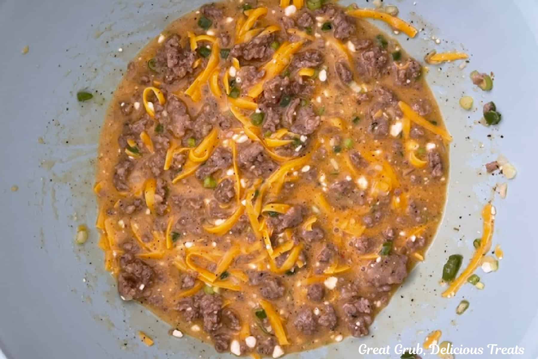 A white bowl with eggs, sausage, cheese, and all the ingredients to make sausage egg bites all mixed together.