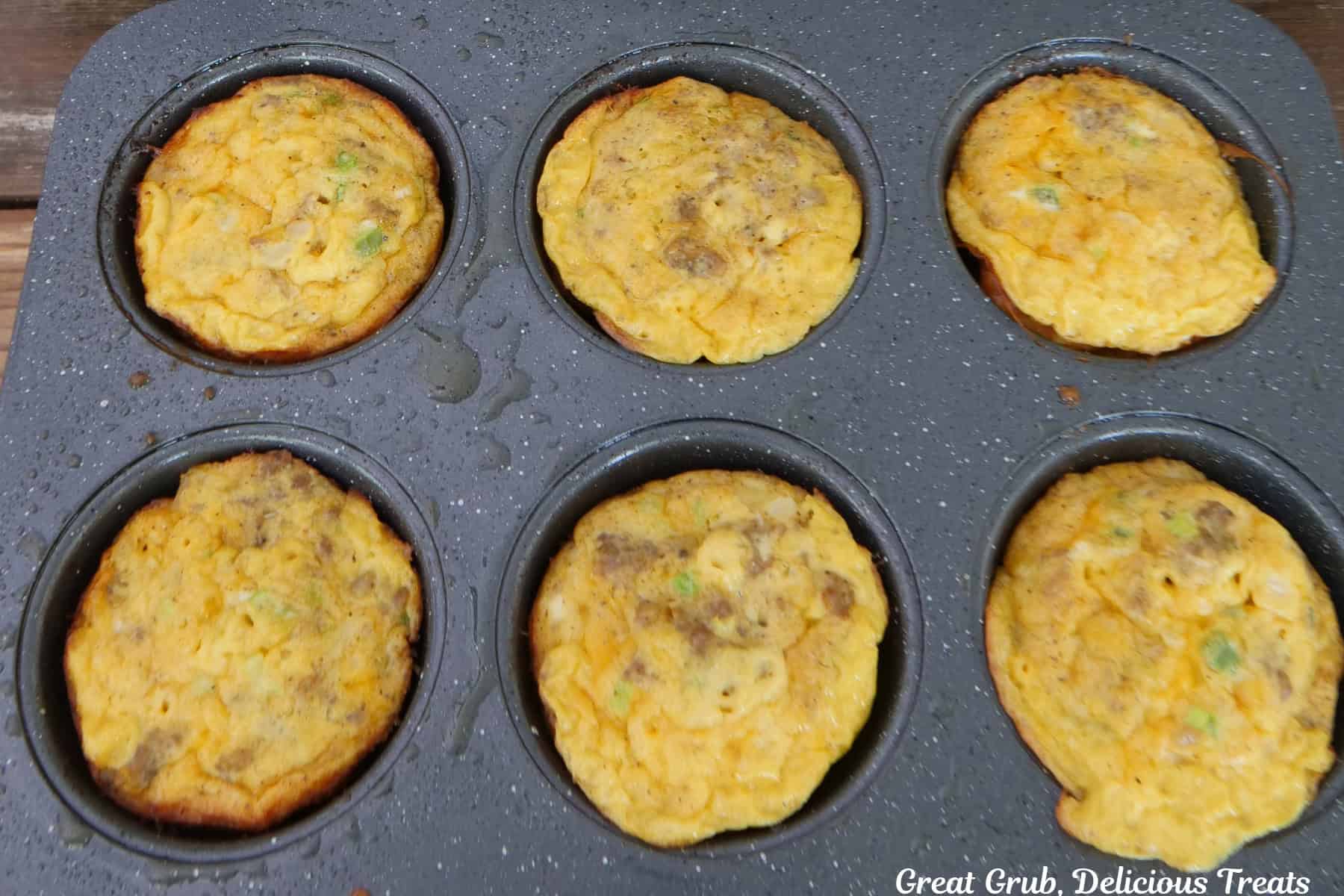 Six baked sausage egg bites in a muffin tin.