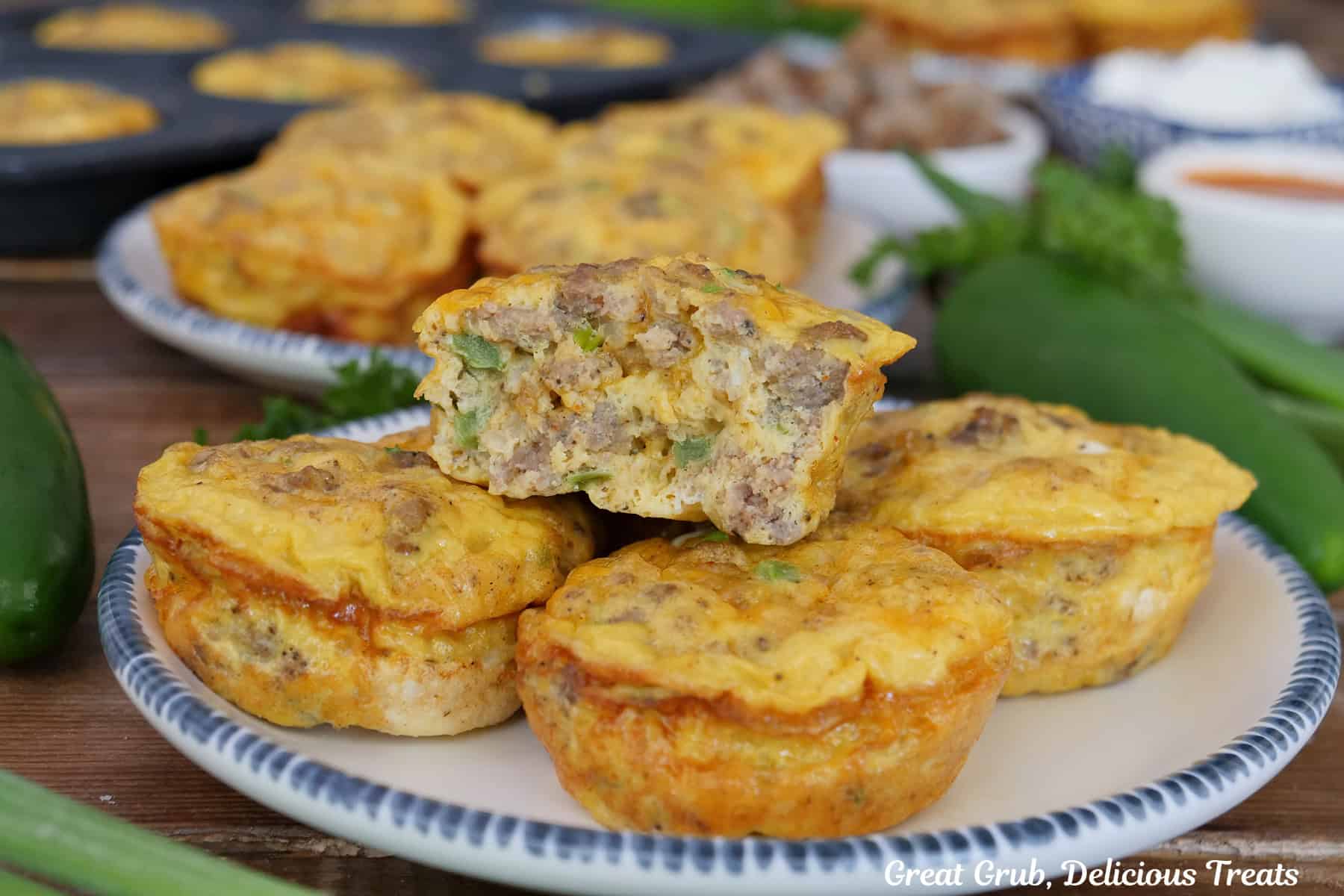 A blue trimmed white plate with five sausage egg bites on it with a bite taken out of the one on top, with more egg bites in the background.