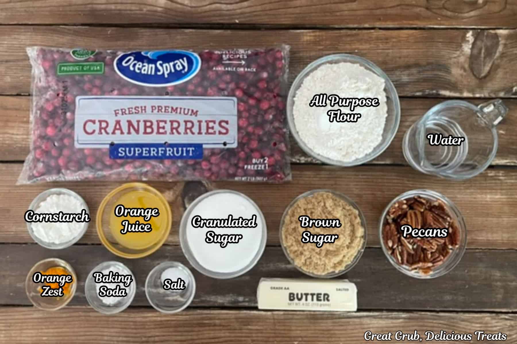 A rustic wood surface with all the ingredients to make sheet pan cranberry orange cobbler placed on it.
