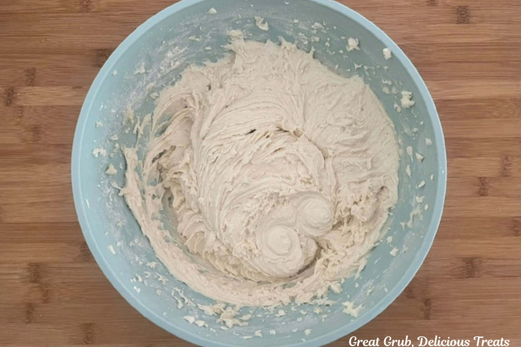 A wood surface with a blue bowl placed on it with cupcake batter in it.