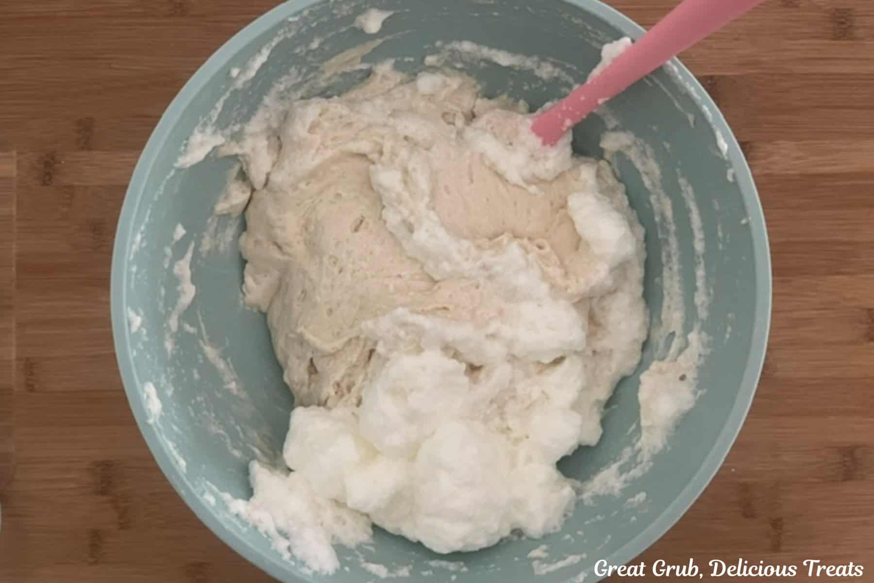 A wood surface with a blue bowl with cupcake batter and egg whites before being mixed together.
