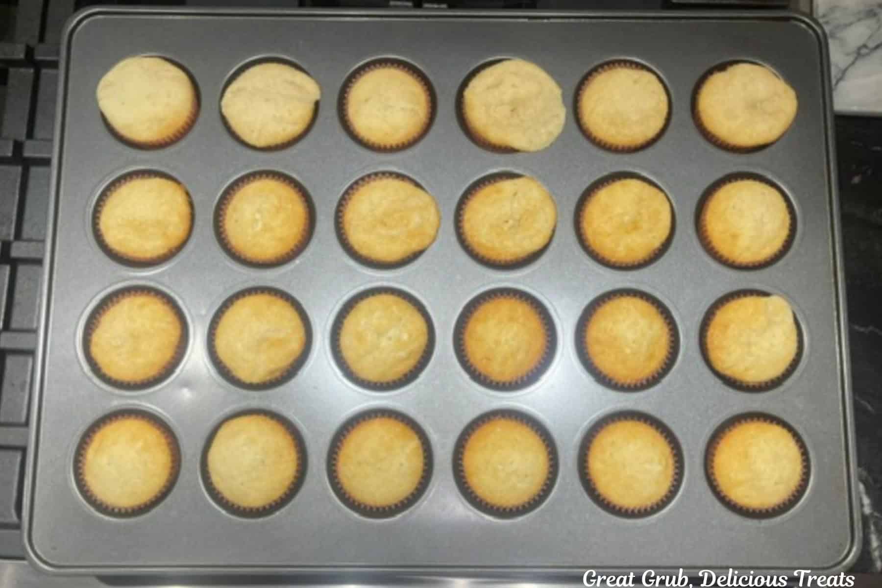 A 24-count cupcake tin with baked white cupcakes in it.