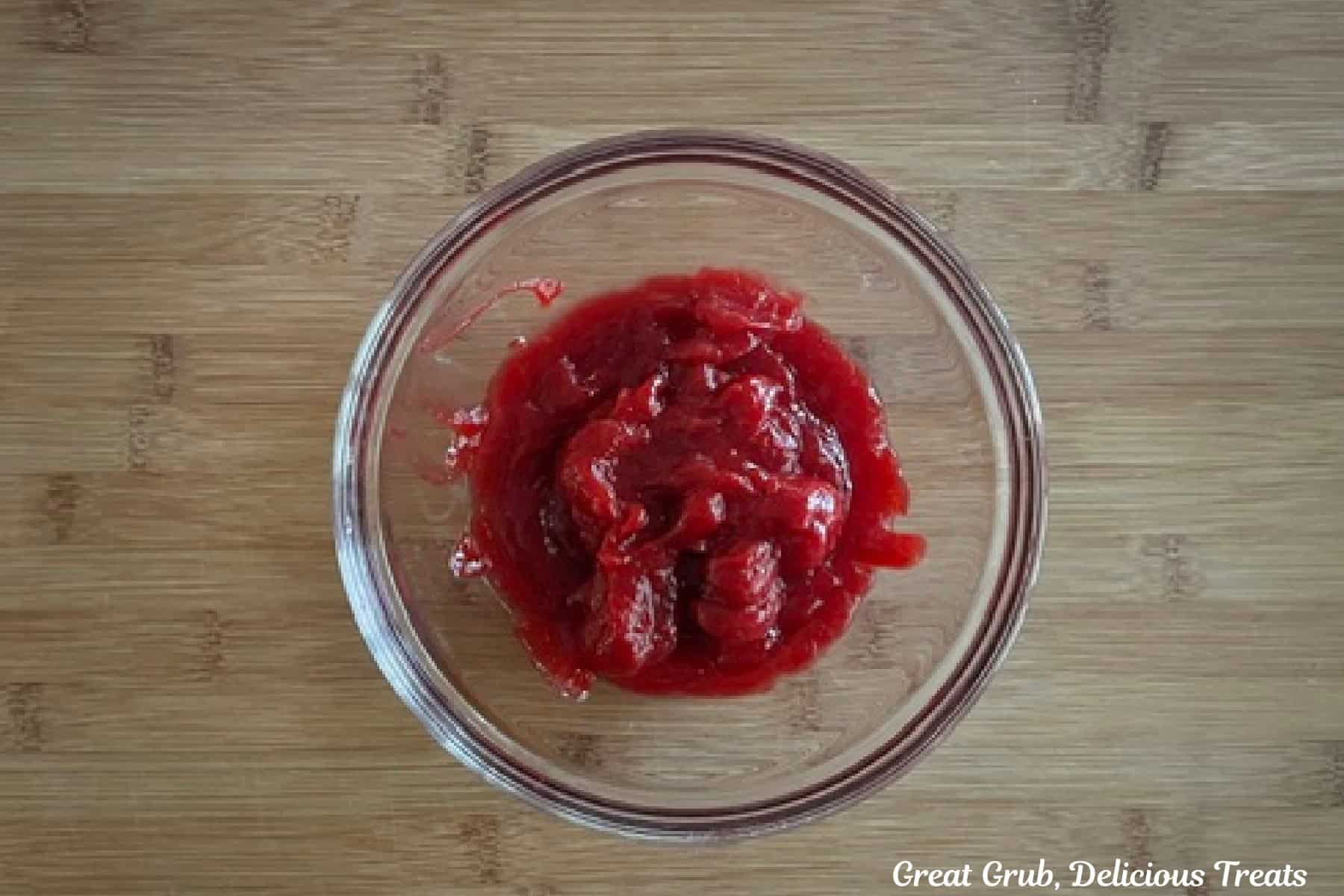 A wood surface with a glass bowl filled with a raspberry filling mixture.