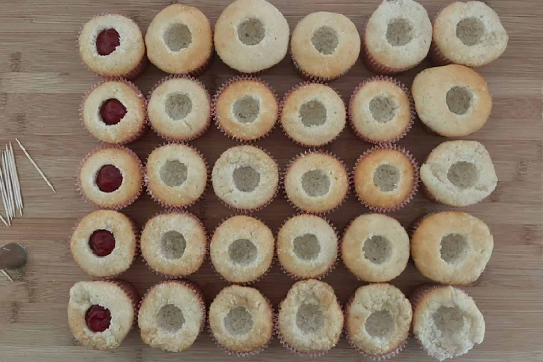 A wood surface with thirty white cupcakes that have the center removed placed on it.