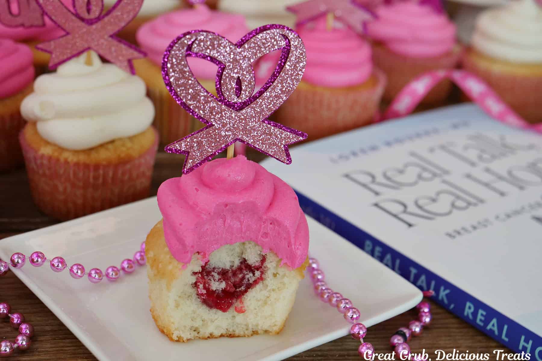 A white cupcake with pink frosting on top with a bite taken out showing the raspberry filling, and Dr. Loren Rourke's book Real Talk, Real Hope in the foreground.