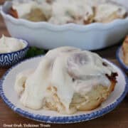 A banana cinnamon roll on a white plate topped with cream cheese icing.