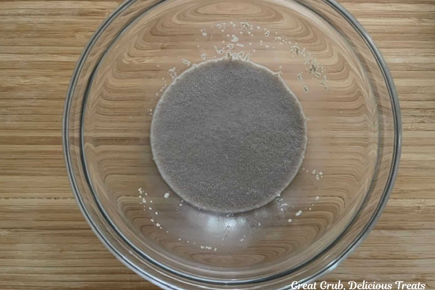 A glass bowl on a wood surface with milk, sugar, and yeast proofing.
