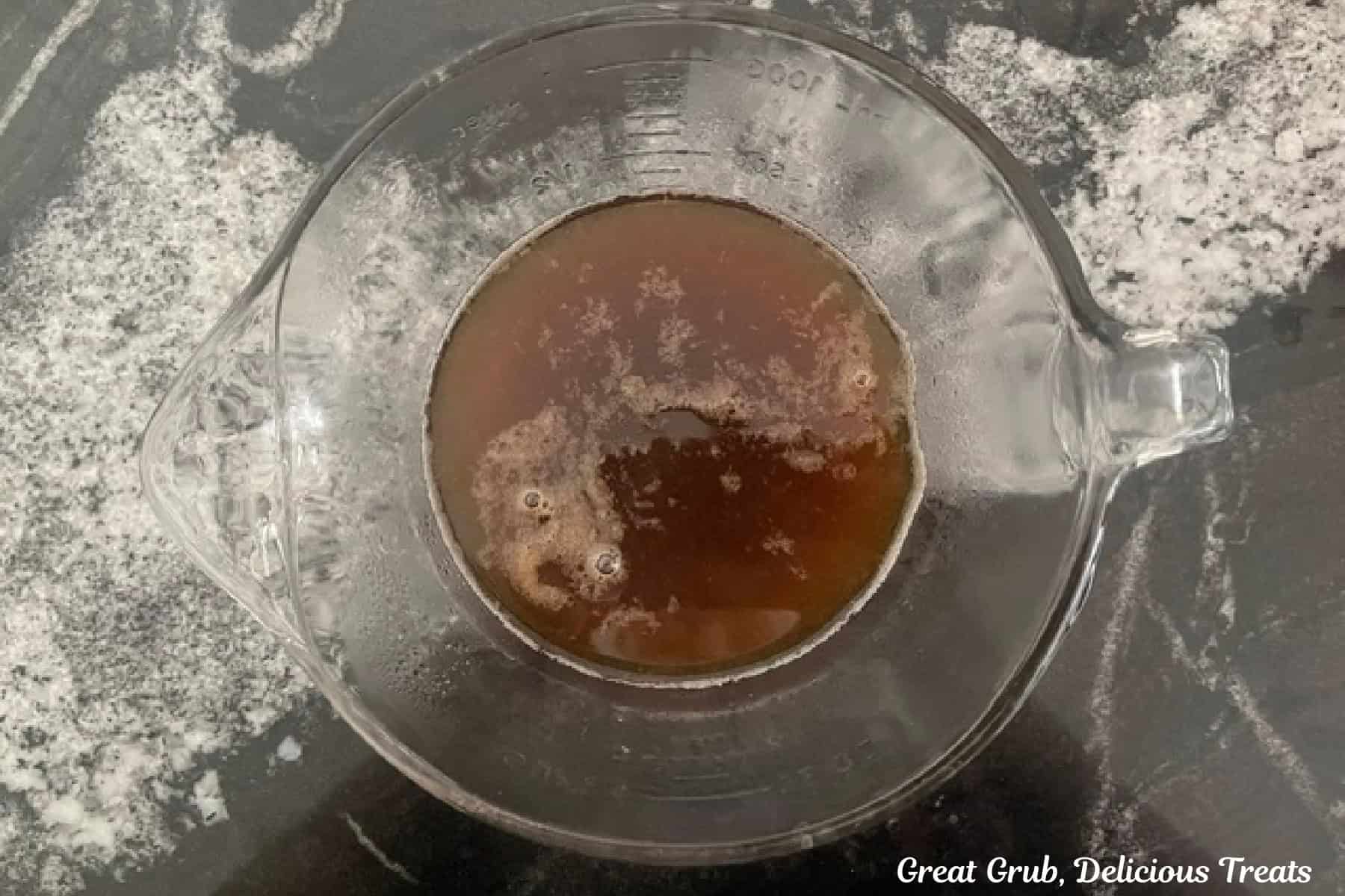 A glass bowl on a black countertop with homemade banana syrup in it.