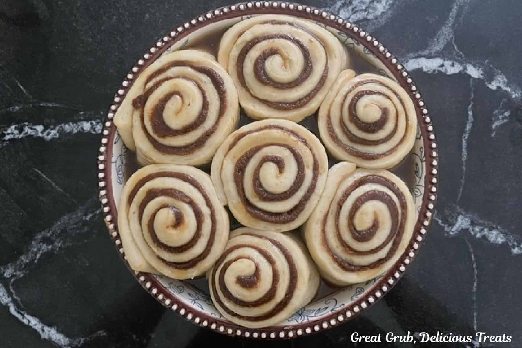 A round baking dish with seven banana cinnamon rolls in it before being baked.