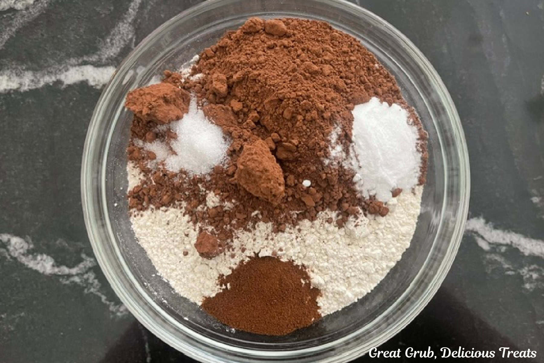 A black countertop with a glass bowl filled with the dry cookie ingredients in it.
