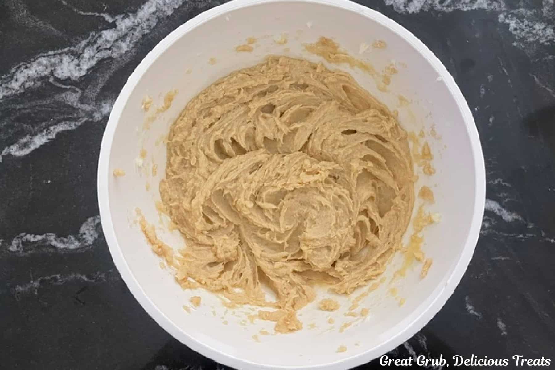 A white bowl filled with combined wet cookie dough ingredients in it.