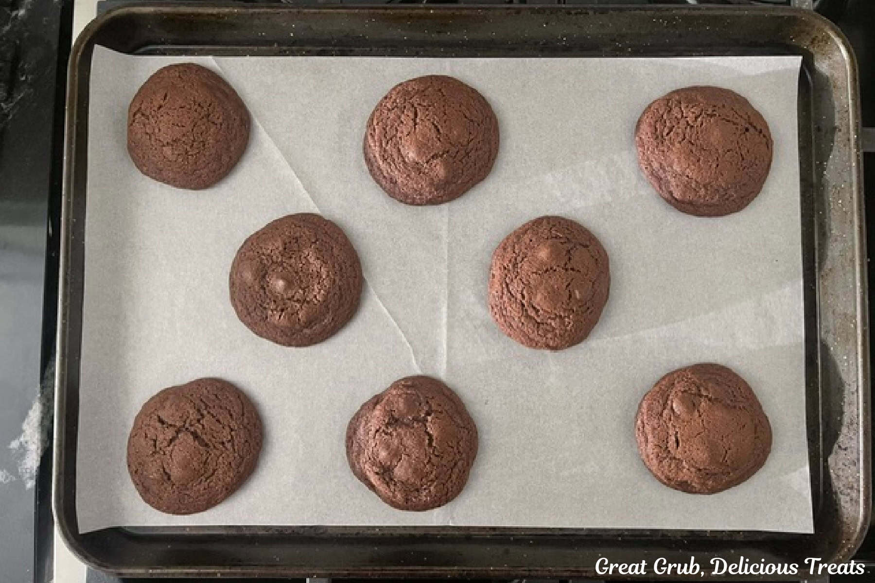 A parchment lined baking sheet with eight baked chocolate cookies on it.
