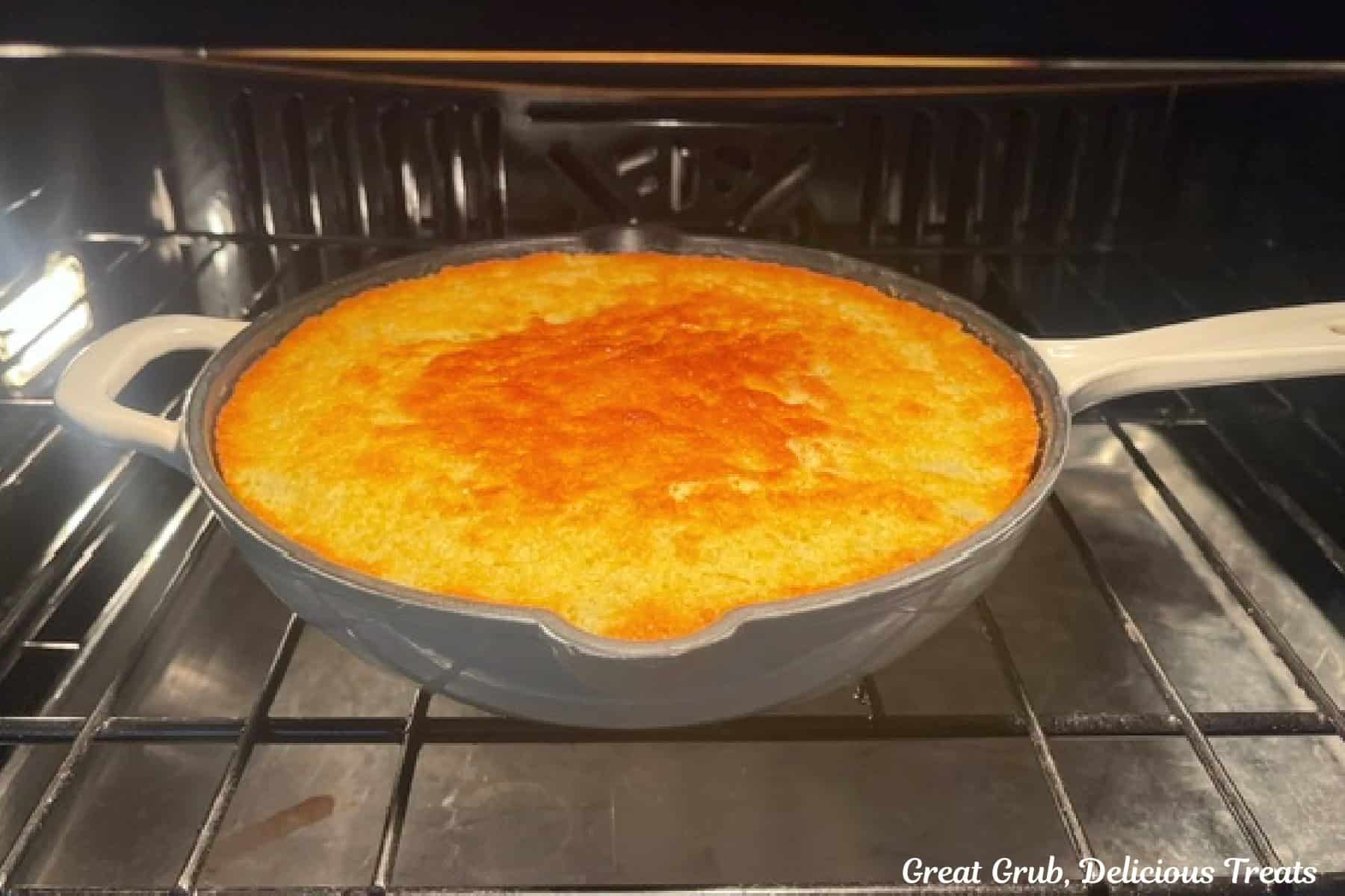 A white cast iron skillet in the oven with jalapeno cornbread baking in it.