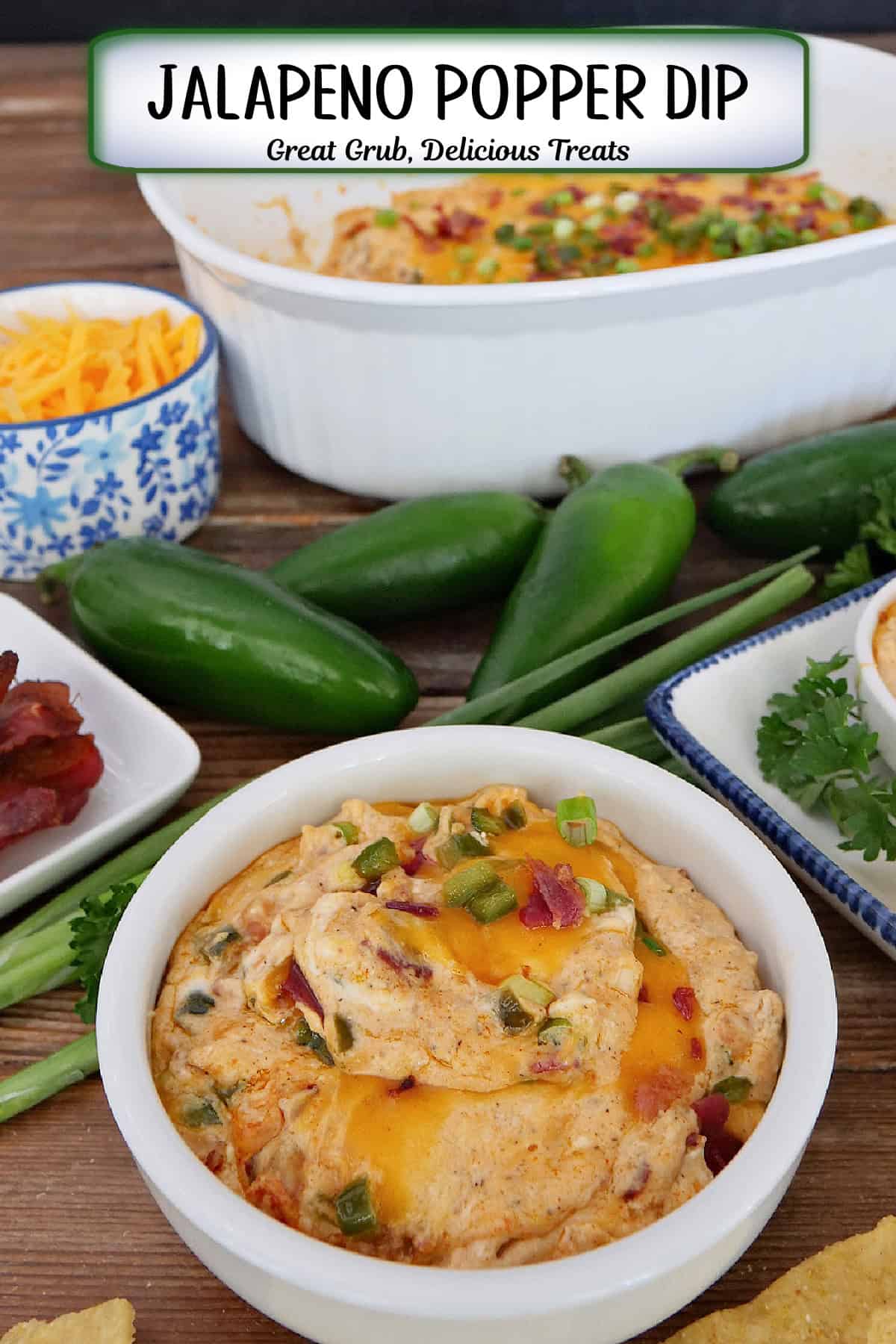 A white bowl filled with jalapeno popper dip with jalapenos, bacon, green onions, shredded cheese in the background, and a title overlay at the top.