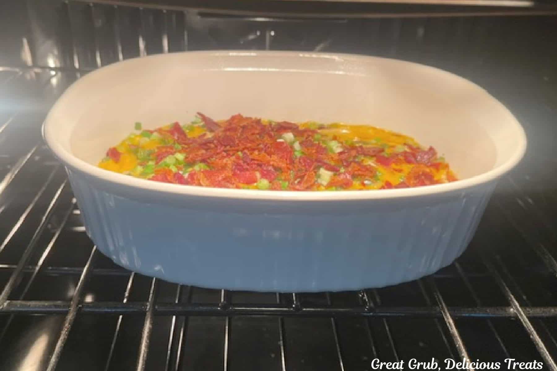 A baking dish in the oven baking jalapeno popper dip.