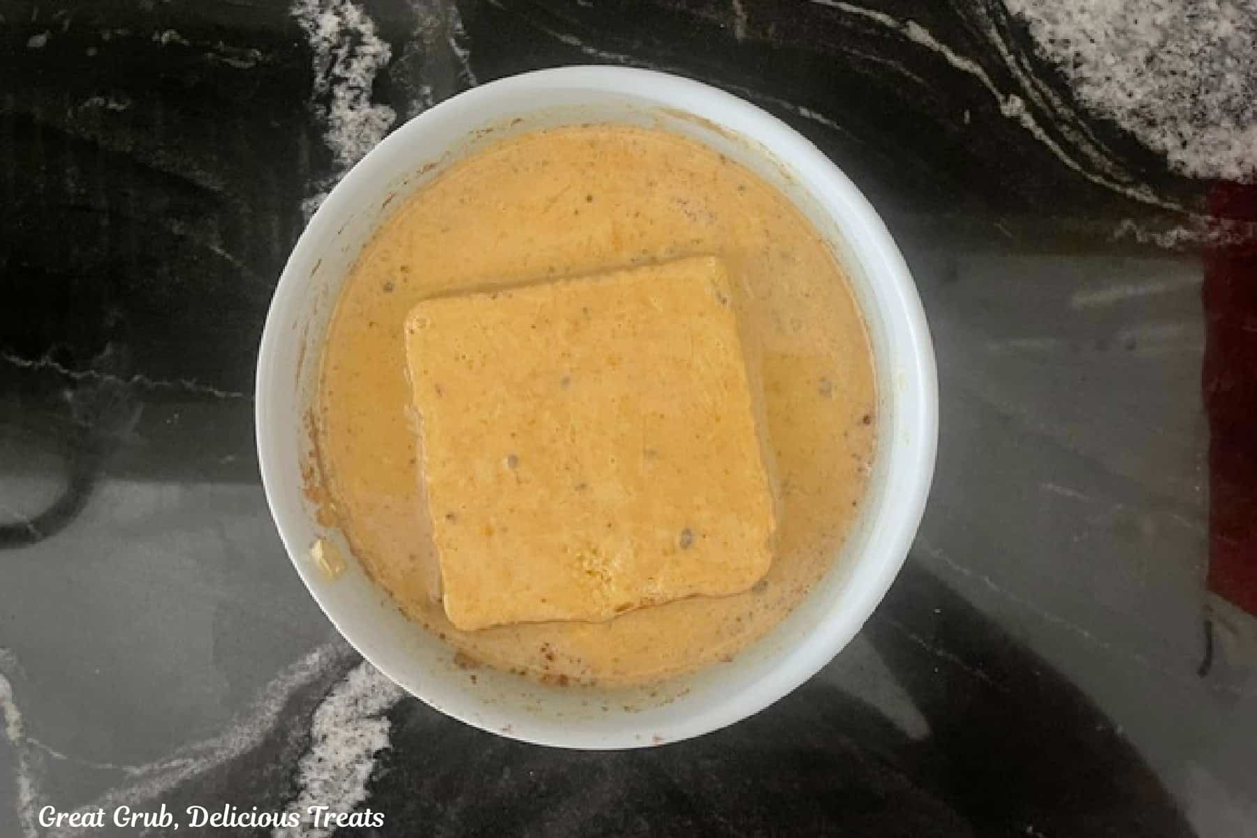 A thick slice of Texas toast bread dipped in pumpkin spice egg mixture in a medium bowl.