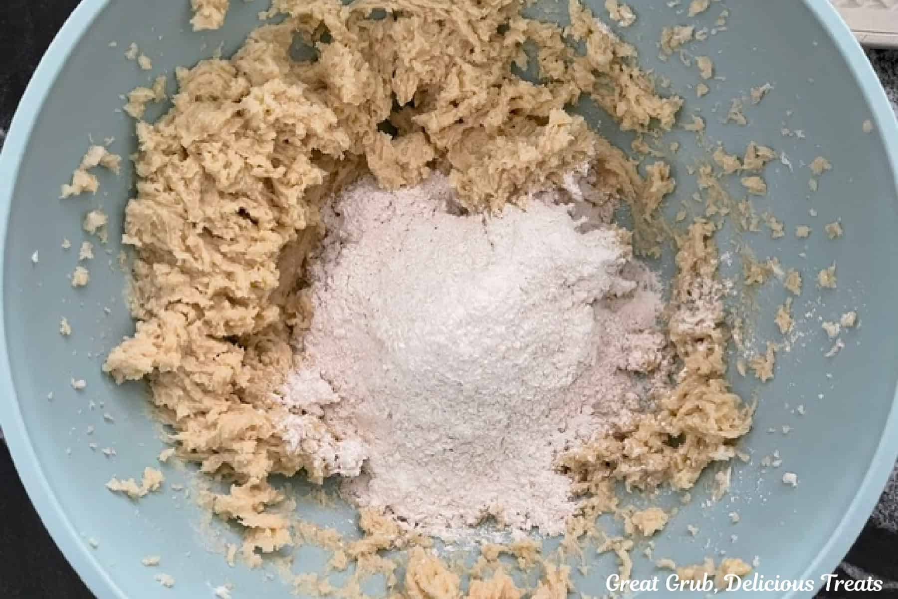 A light blue bowl with the dry cookie ingredients added to the wet cookie batter.