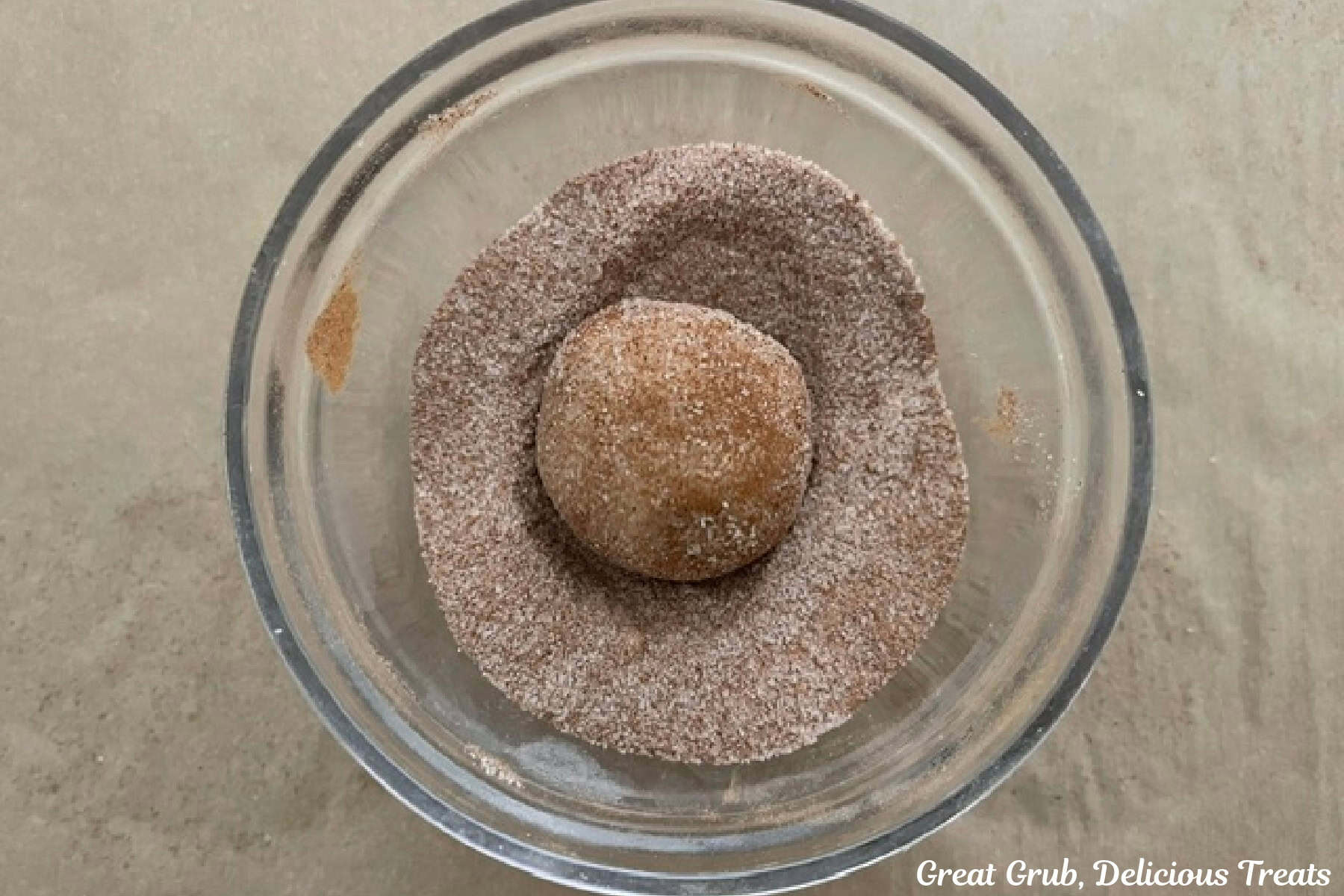 A glass bowl filled with cinnamon and sugar and a cookie dough ball rolled in the mixture.
