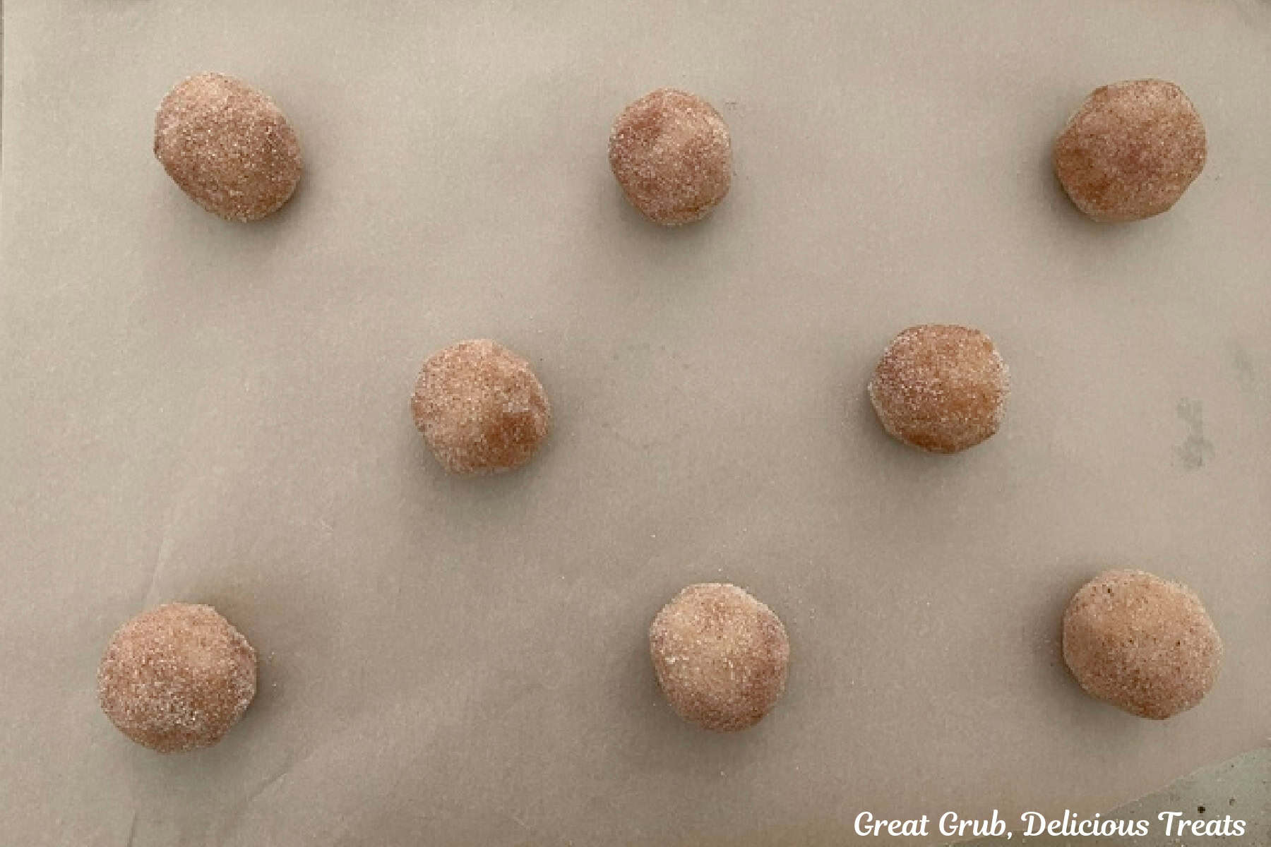 A parchment lined baking sheet with eight cookie dough balls on it before being baked.