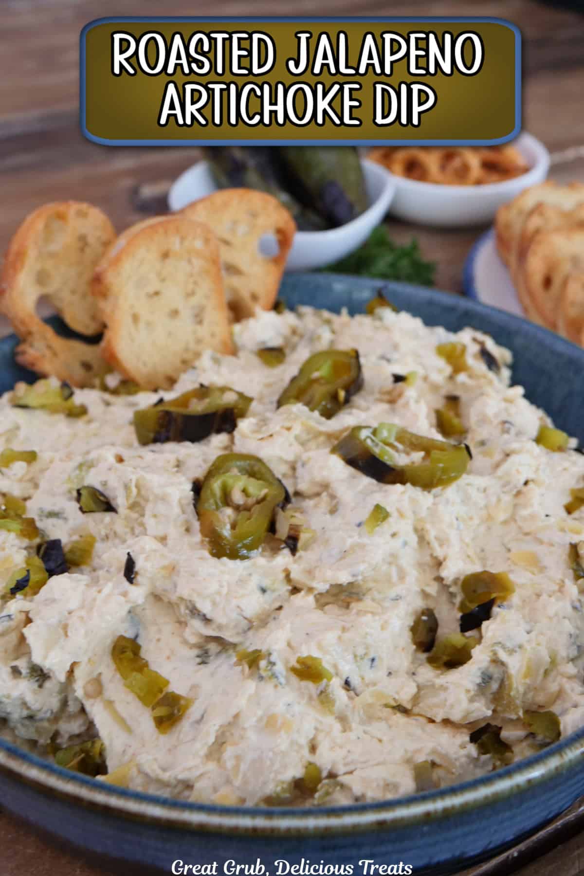 A blue bowl filled with roasted jalapeno artichoke dip with three crusty pieces on bread stuck in the dip, and a title overlay at the top.